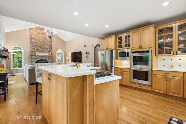 kitchen with lofted ceiling, backsplash, a kitchen island with sink, a brick fireplace, and stainless steel appliances