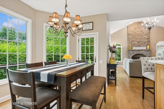 dining room featuring vaulted ceiling, light hardwood / wood-style floors, a notable chandelier, and a brick fireplace