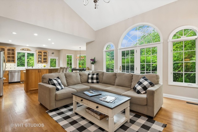 living room with light wood-type flooring, high vaulted ceiling, an inviting chandelier, and a wealth of natural light