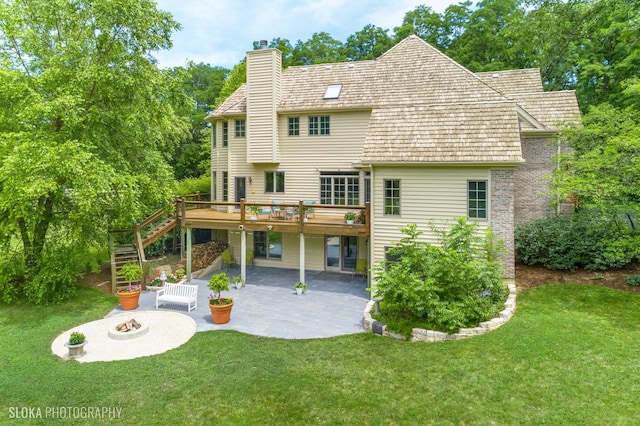 rear view of house with a lawn, a wooden deck, a patio, and an outdoor fire pit