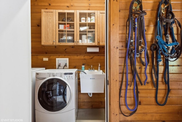 clothes washing area with washer and dryer, wood walls, cabinets, and sink