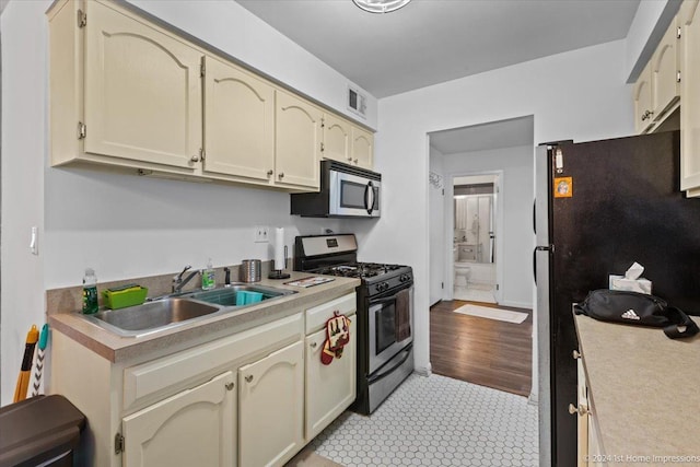 kitchen with appliances with stainless steel finishes, sink, light tile patterned floors, and cream cabinets