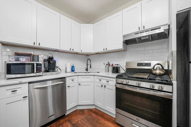 kitchen with dark hardwood / wood-style floors, appliances with stainless steel finishes, white cabinets, tasteful backsplash, and sink