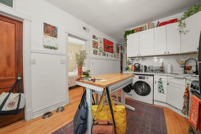 kitchen with white cabinetry, gas range, washer / clothes dryer, light wood-type flooring, and tasteful backsplash