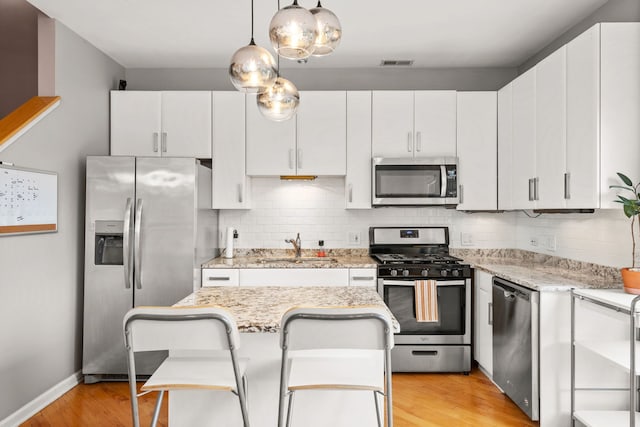 kitchen featuring white cabinetry, stainless steel appliances, light hardwood / wood-style floors, and backsplash