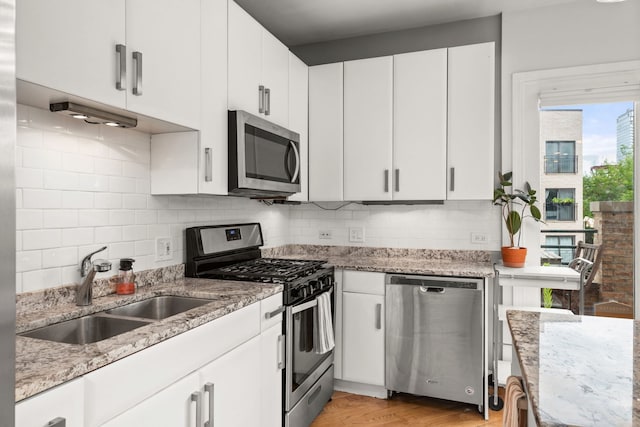 kitchen with white cabinets, light hardwood / wood-style floors, decorative backsplash, and appliances with stainless steel finishes