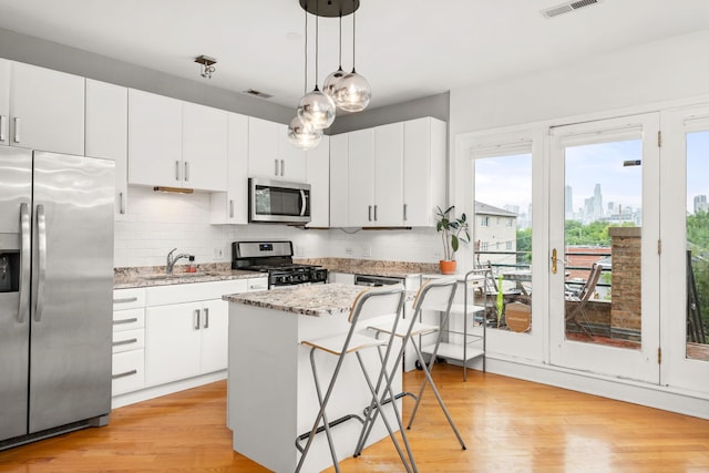 kitchen featuring white cabinets, decorative backsplash, light hardwood / wood-style floors, appliances with stainless steel finishes, and a breakfast bar