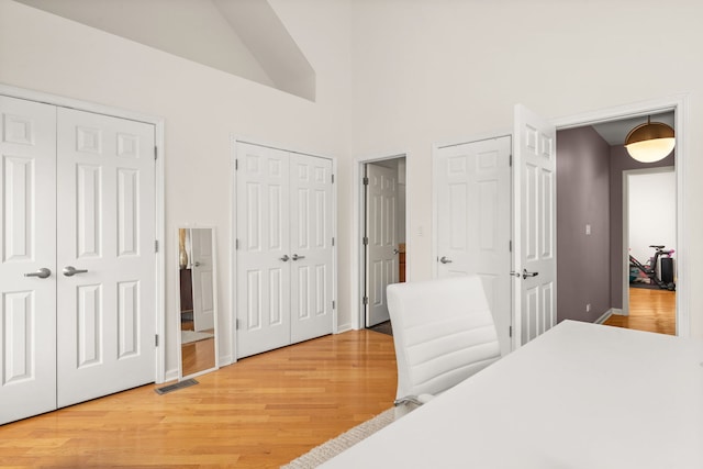 bedroom with light hardwood / wood-style floors, high vaulted ceiling, and two closets