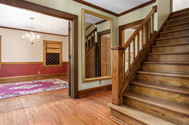 stairs featuring an inviting chandelier, wood-type flooring, and ornamental molding