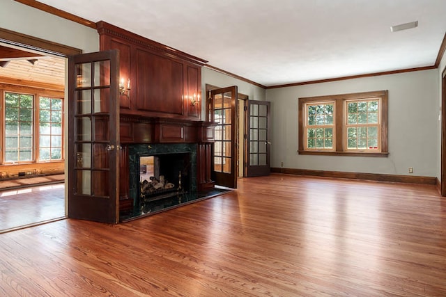 unfurnished living room with hardwood / wood-style flooring, crown molding, a premium fireplace, and french doors