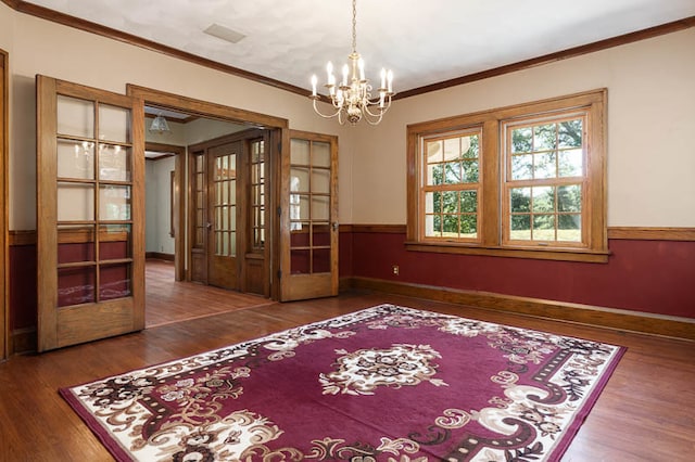 spare room with wood-type flooring, french doors, ornamental molding, and an inviting chandelier