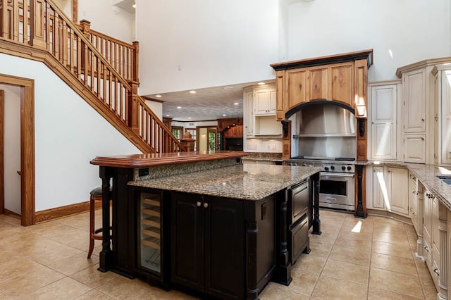 kitchen with a kitchen bar, dark stone counters, light tile patterned floors, a kitchen island, and a towering ceiling