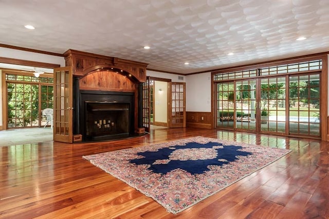 unfurnished living room featuring french doors, crown molding, hardwood / wood-style floors, and a large fireplace