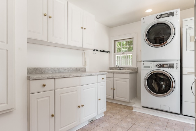 clothes washing area featuring stacked washer and dryer, sink, cabinets, and light tile patterned floors