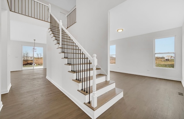 stairway with a wealth of natural light, a towering ceiling, and dark wood-type flooring