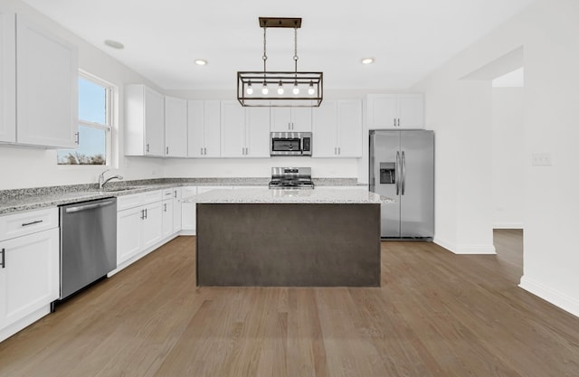 kitchen with white cabinets, dark wood-type flooring, a kitchen island, stainless steel appliances, and light stone countertops