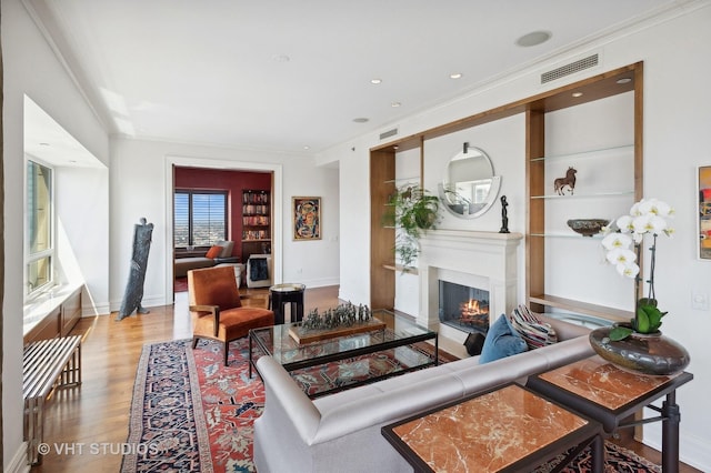 living room with built in shelves, crown molding, and light hardwood / wood-style flooring