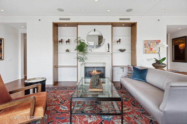 living room featuring hardwood / wood-style flooring, built in shelves, a large fireplace, and ornamental molding