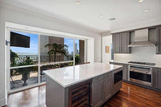 kitchen featuring appliances with stainless steel finishes, beverage cooler, dark wood-type flooring, wall chimney range hood, and a kitchen island