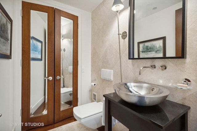 bathroom featuring backsplash, french doors, sink, toilet, and tile walls