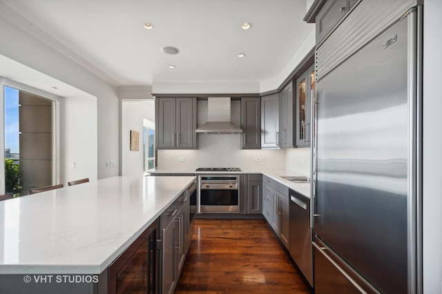 kitchen featuring appliances with stainless steel finishes, dark hardwood / wood-style flooring, light stone counters, wall chimney exhaust hood, and wine cooler