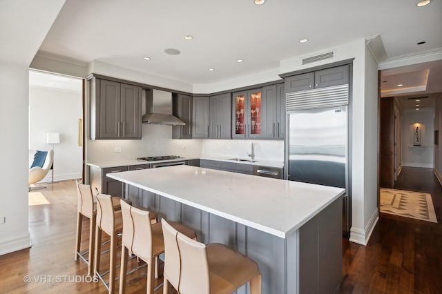 kitchen featuring stainless steel appliances, wall chimney range hood, dark hardwood / wood-style flooring, gray cabinets, and a kitchen island