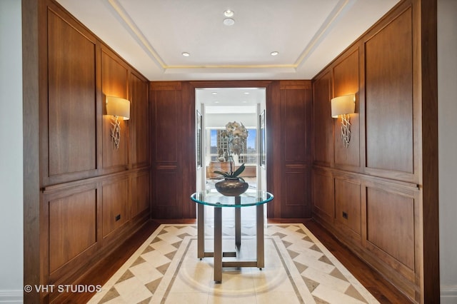 hallway with a tray ceiling and wooden walls