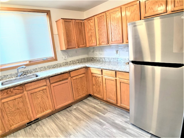 kitchen with sink, stainless steel refrigerator, light stone countertops, and light wood-type flooring