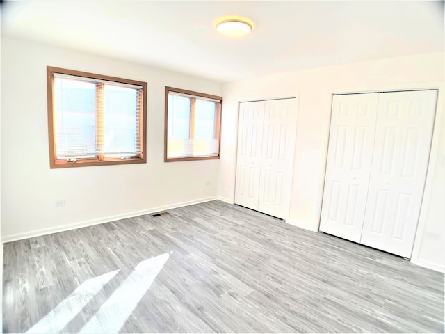 unfurnished bedroom with light hardwood / wood-style floors and two closets