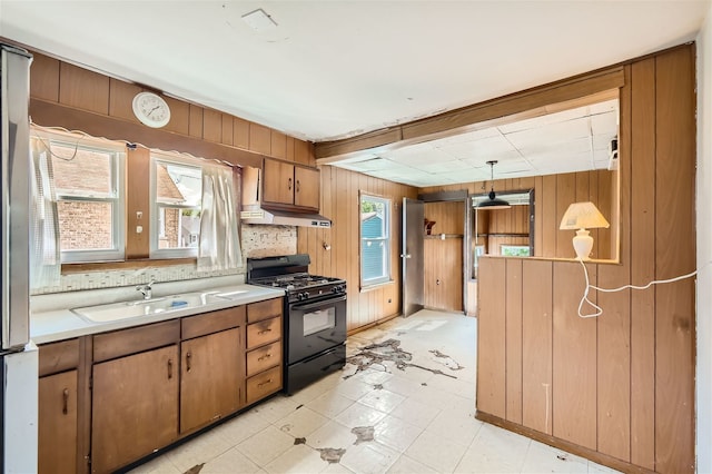 kitchen with decorative light fixtures, wood walls, black range with gas cooktop, and a wealth of natural light