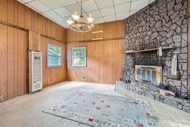 unfurnished living room with carpet flooring, an inviting chandelier, a stone fireplace, and wood walls