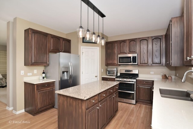 kitchen with decorative light fixtures, sink, a center island, appliances with stainless steel finishes, and light hardwood / wood-style flooring