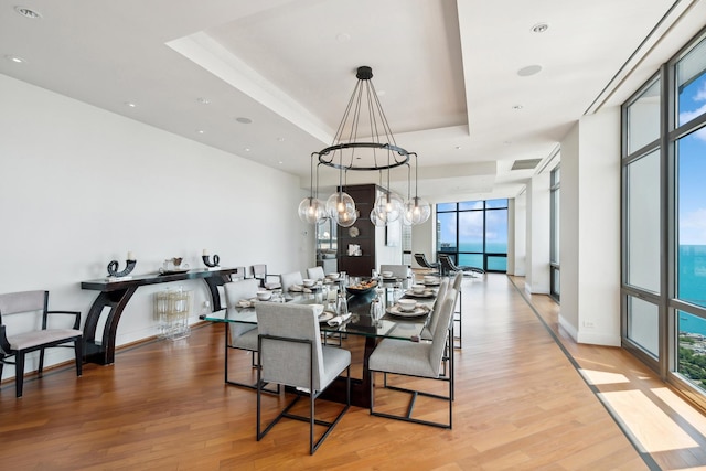 dining space with a tray ceiling, light hardwood / wood-style flooring, a notable chandelier, and a wall of windows