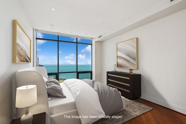 bedroom featuring floor to ceiling windows, a water view, and dark wood-type flooring