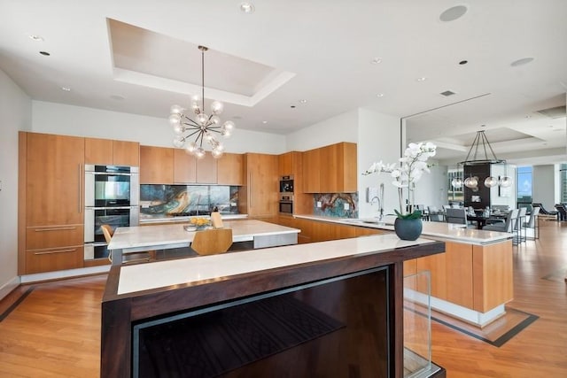 kitchen with pendant lighting, a spacious island, double oven, and a tray ceiling