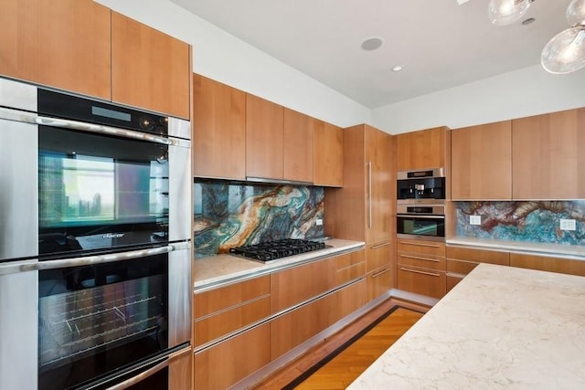 kitchen featuring light wood-type flooring, backsplash, stainless steel appliances, and light stone countertops