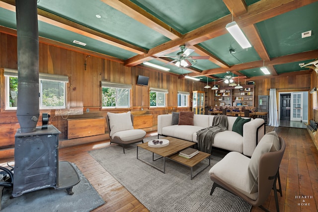 living room with beamed ceiling, coffered ceiling, a wood stove, ceiling fan, and dark hardwood / wood-style floors