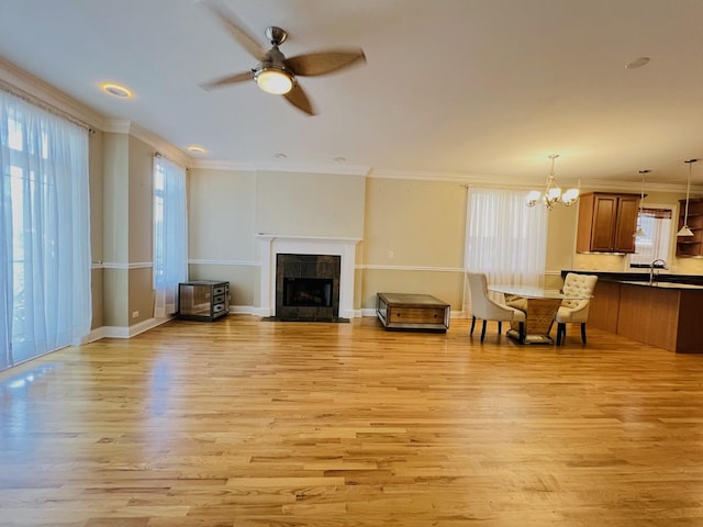 living room with ceiling fan with notable chandelier, plenty of natural light, light wood-type flooring, and crown molding