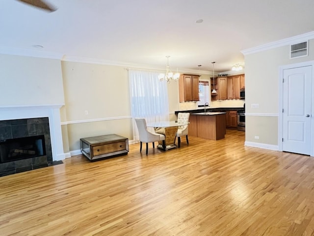 living room with a tiled fireplace, light hardwood / wood-style floors, a notable chandelier, and ornamental molding