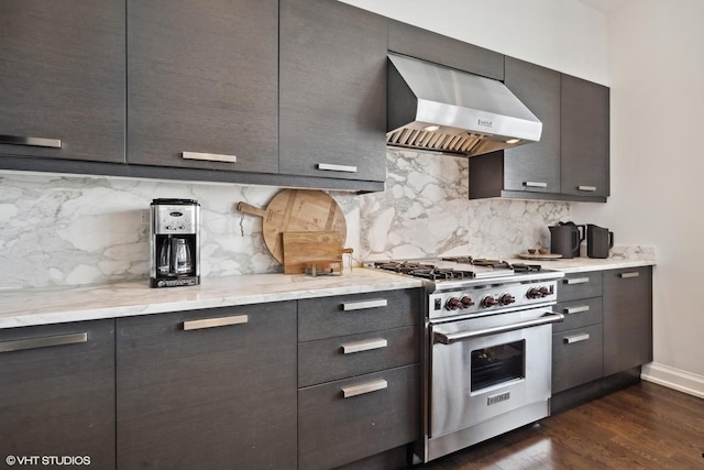 kitchen featuring tasteful backsplash, wall chimney range hood, high end range, light stone countertops, and dark wood-type flooring