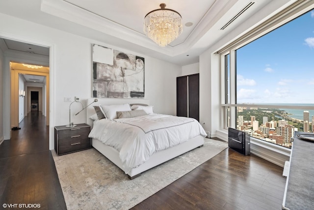 bedroom featuring wood-type flooring, a tray ceiling, a notable chandelier, and a water view