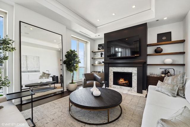 living room with a high end fireplace, crown molding, hardwood / wood-style flooring, and a tray ceiling