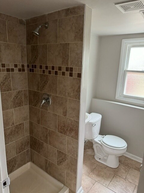 bathroom with tiled shower, toilet, and tile patterned floors