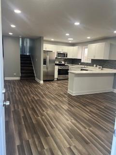 kitchen with appliances with stainless steel finishes, kitchen peninsula, backsplash, dark hardwood / wood-style floors, and white cabinetry