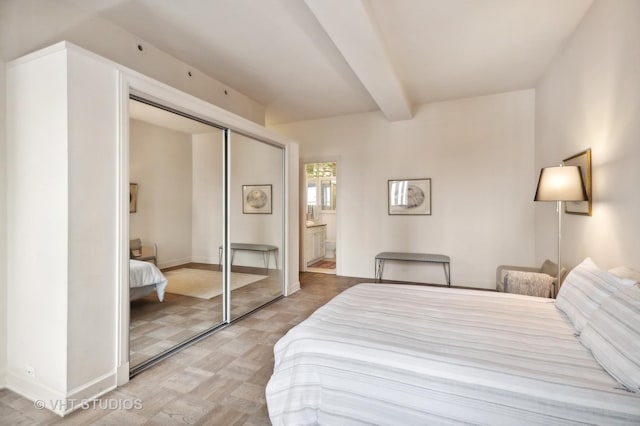 bedroom with a closet, baseboards, beamed ceiling, and ensuite bathroom