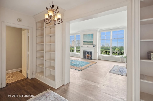 interior space with an inviting chandelier, a lit fireplace, built in features, and wood finished floors