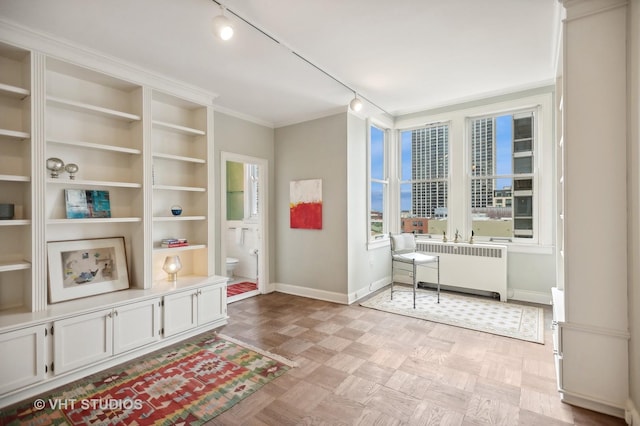 living area with track lighting, baseboards, radiator, a view of city, and crown molding