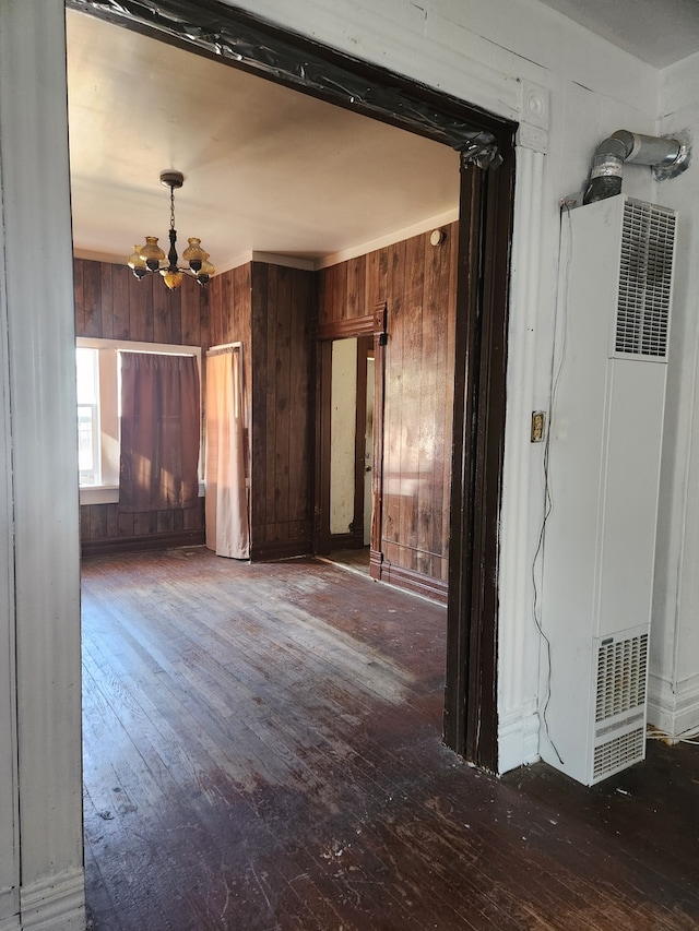 spare room featuring dark hardwood / wood-style floors, wooden walls, and a chandelier