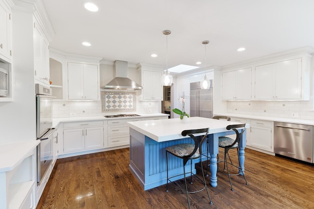 kitchen featuring wall chimney range hood, pendant lighting, built in appliances, dark hardwood / wood-style floors, and white cabinetry