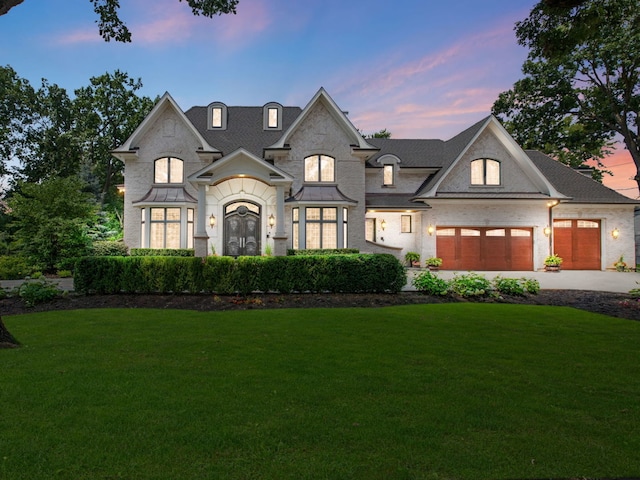 french country inspired facade featuring a front yard, a standing seam roof, driveway, and an attached garage